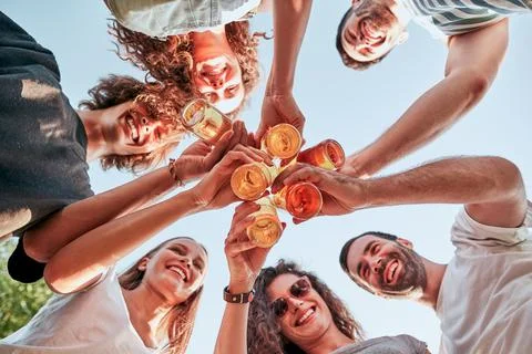 Down view image of a group of happy friends clinking beer bottles standing to Stock Photos