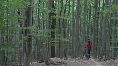 Downhill mountain biker resting at the start of a trail in a green forest. 스톡 동영상 53871269