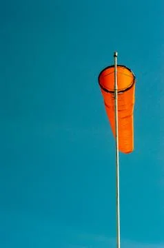 Downward angled plain orange windsock against a clear blue sky. Stock Photos