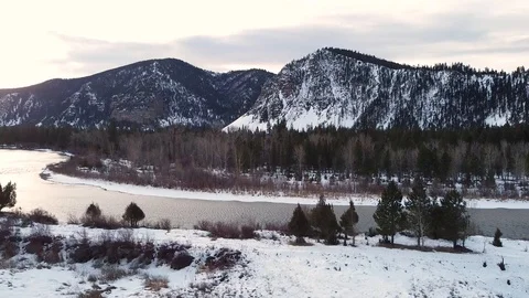 Downward crane shot of snow covered field with trees and river in front of ta Stock Footage 125401618