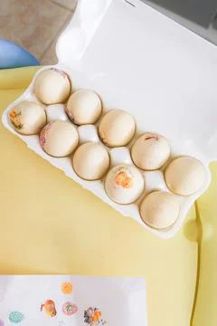 A dozen eggs are sitting in a white carton on a yellow table Stock Photos