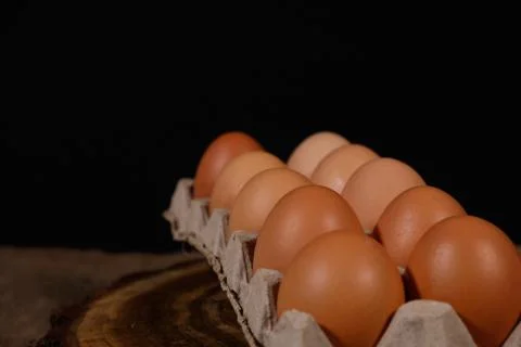A dozen eggs in a cardboard open box on a black background side view. Stock Photos