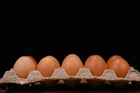 A dozen eggs in a cardboard open box on a black background side view. Stock Photos