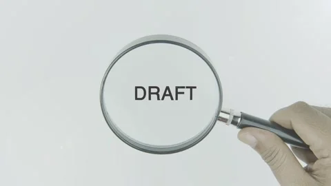 Draft text or word highlighted by a magnifying glass in a hand on a white Stock Footage 303615020