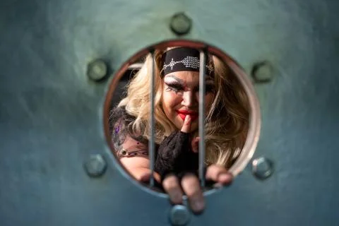 Drag queen posing close to iron grate, which looks like prisons. A wig with Stock Photos