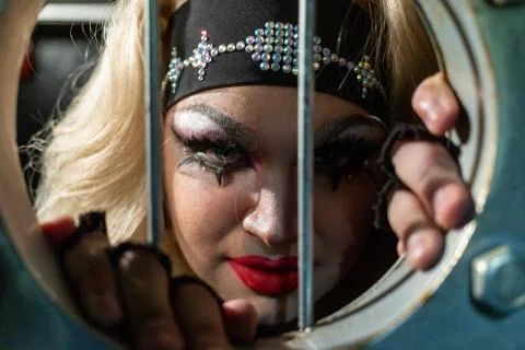 Drag queen posing close to iron grate, which looks like prisons. A wig with 库存照片