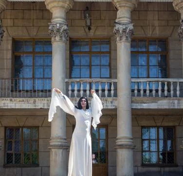 Drag queen posing close to old building in white dress. A wig with Black long Stock Photos