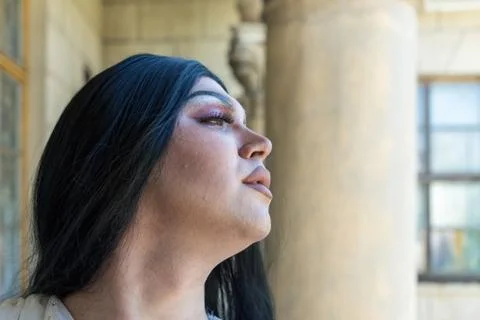 Drag queen posing close to old building in white dress. A wig with Black long Stock Photos