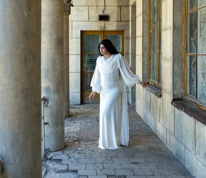 Drag queen posing close to old building in white dress. A wig with Black long 스톡 사진