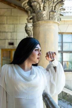 Drag queen posing close to old building in white dress. A wig with Black long Stock-Fotos
