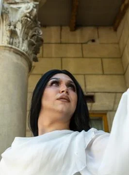 Drag queen posing close to old building in white dress. A wig with Black long Foto stock