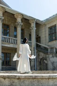 Drag queen posing close to old building in white dress. A wig with Black long Stock-Fotos