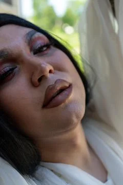 Drag queen posing close to old building in white dress. A wig with Black long Stock Photos