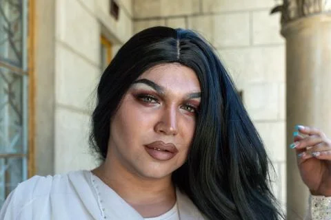 Drag queen posing close to old building in white dress. A wig with Black long 库存照片