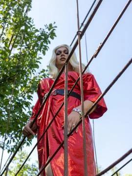 Drag queen posing on a iron construction in red dress. A wig with white long Stock Photos