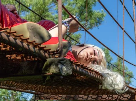 Drag queen posing on a iron construction in red dress. A wig with white long Stock Photos