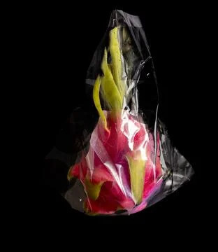 Dragon fruit wrapped in transparent plastic bag on black background. Creative Stock Photos