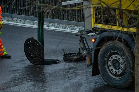 Drain cleaning worker is standing in front of an open manhole cover, doing his Stock Photos