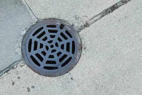 Drain cover on concrete sidewalk with pattern seen on a sunny day in the city Stock Photos