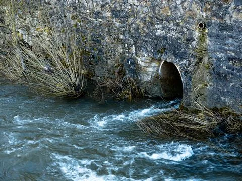 A drain that is embedded in a wall and flows into a river Stock-Fotos