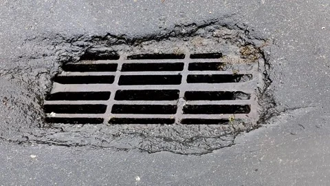 Drain grate on wet asphalt road surface with water flowing into opening, Stock Footage 344094086