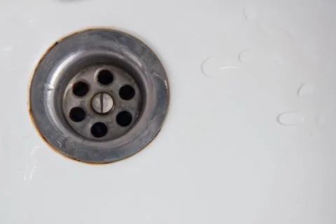 Drain hole with rust around the edges in a white sink or bathtub with drops o Stock Photos