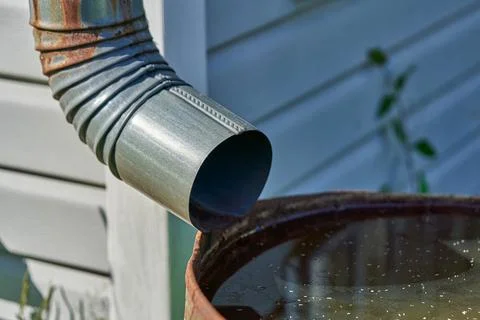The drain pipe is connected to a rusty iron barrel with rainwater Stock Photos