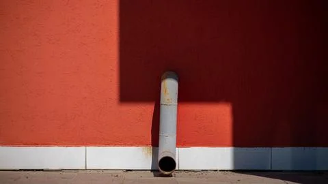 Drain pipe on red wall with geometric shadows Stock Photos