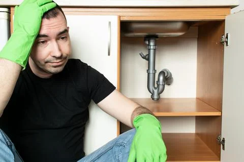 Drain Problems, blockage plumbing kitchen sink pipe unclog male man sit tired Stock Photos