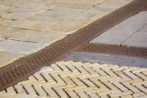 A drainage ditch covered with an iron patterned lattice on a sidewalk. Stock Photos