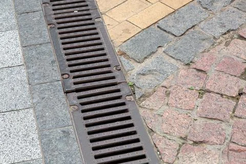 Drainage grate of a storm system on pedestrian sidewalk made of stone tiles. Stock Photos