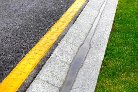 Drainage system edge tray with stream rain water near an asphalt road. Stock Photos