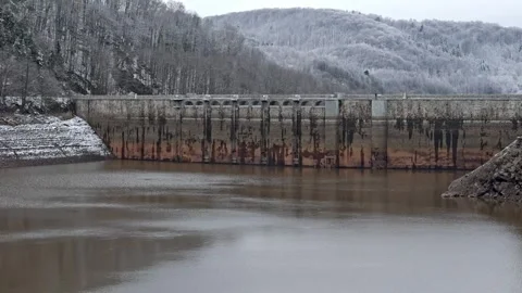 A drained lake exposes its dam and deeply receded banks, with a snow-covere.. Stock Footage 296000668