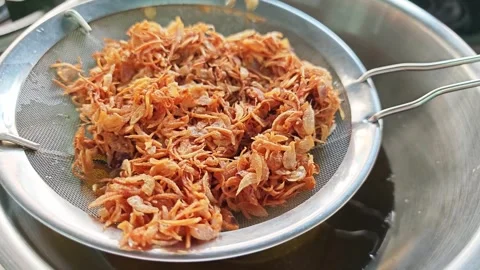 Draining freshly fried crispy shallots in a stainless steel strainer. Stock Footage 346533101