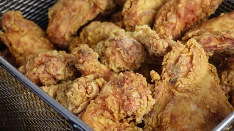 Draining golden bone-in fried chicken from hot oil in a commercial fryer basket Stock Footage 340566582