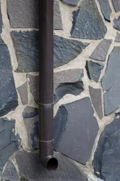 Drainpipe on the background of stone blocks of different colors. Stock Photos