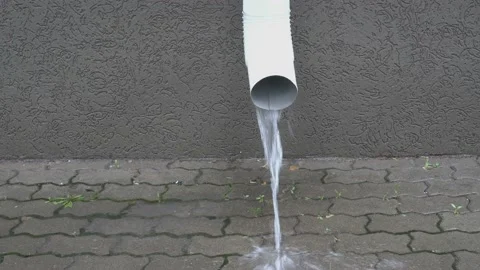 A drainpipe on the facade of the building pours a stream of water Видео 116442413