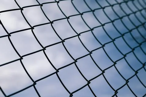 Dramaic blue sky with white clouds through a metal grid chain fence Stock Photos