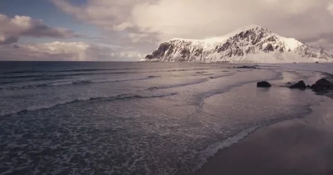 Dramatic 4K Ocean Waves Washing Ashore Near Snowy Mountain Peak Stock Footage 323835587
