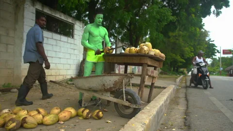 Dramatic 4k video of painted green man chopping coconuts in Caribbean coast. Stock Footage 142475898