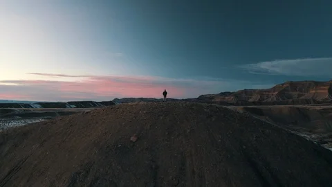Dramatic aerial of lone man standing atop snowy hill at sunset Stock Footage 124813101