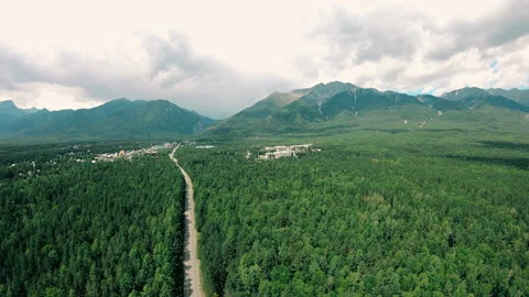Dramatic aerial view of mountains, dark green forest landscape, road and town Stock Footage 92324156