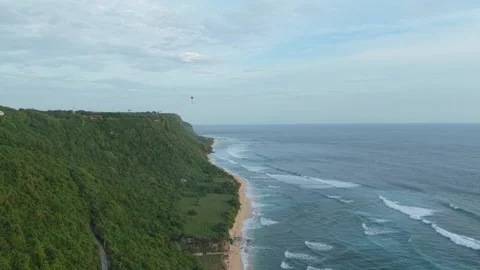 Dramatic aerial view of paragliders soaring over a lush green cliff and sandy 動画素材 328595427