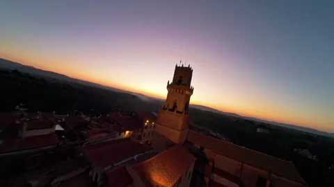 Dramatic aerial view of tall stone bell tower rising above red-tiled village Stock Footage 330254309