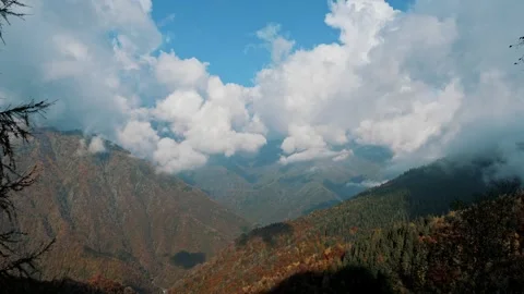 Dramatic alpine panorama with forested mountain ridges under fluffy white clouds Stock Footage 324961363
