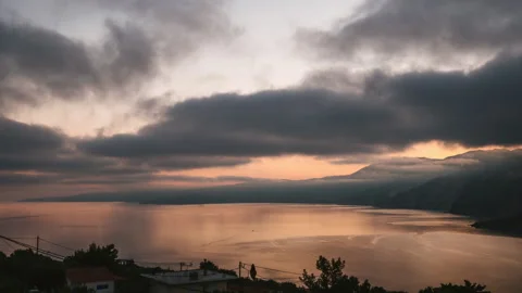 Dramatic and moody time lapse shot of sunrise over rocky shore and calm sea on Stock Footage 341465814