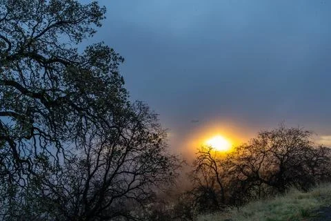 A dramatic atmosphere as the sun glows behind a thick of clouds Stock Photos
