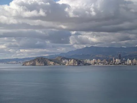 Dramatic atmospheric imagery with soaring clouds over coastal cityscape and Stock Photos