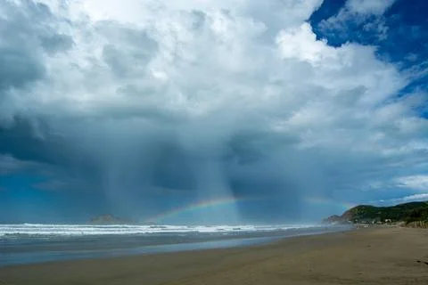 Dramatic Beach Scene with Rainbow and Rainfall Stock Photos