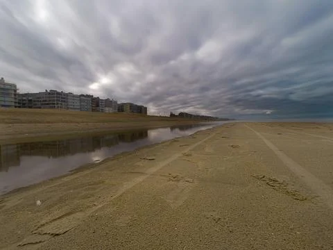 Dramatic Beach Scene with Reflections and Residential Buildings under Overc.. Stock Photos